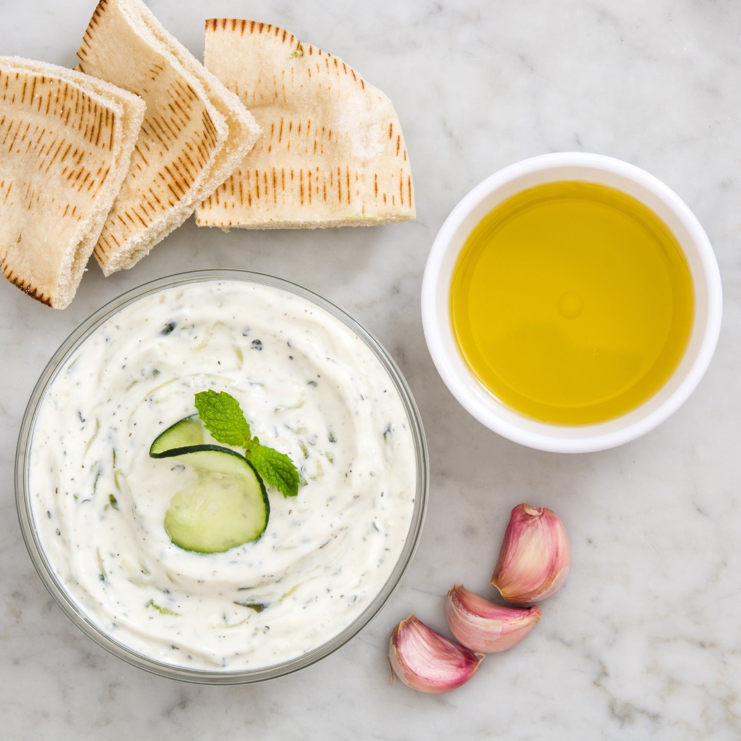 Pasolivo Spring Herb Dip Recipe on a counter next to pita bread, Pasolivo Olive Oil, and garlic cloves