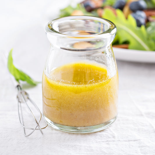 Easy Everyday Salad Dressing recipe in a clear jar on a table with salad and whisk