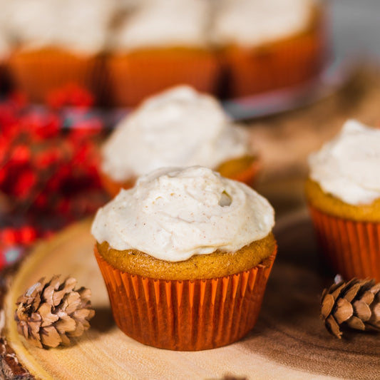 Pasolivo Pumpkin Cupcakes with Sugar & Spice Cream Cheese Frosting Recipe on a table next to pinecone decorations