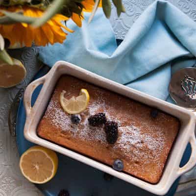 Pasolivo Limoncello Pound Cake Recipe on a table with flowers, garnished with fresh berries and lemon slices