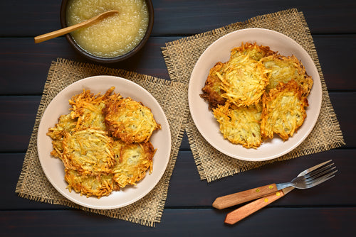 Pasolivo Potato Latkes with Spiced Applesauce Recipe on placemats next to a bowl of applesauce and silverware