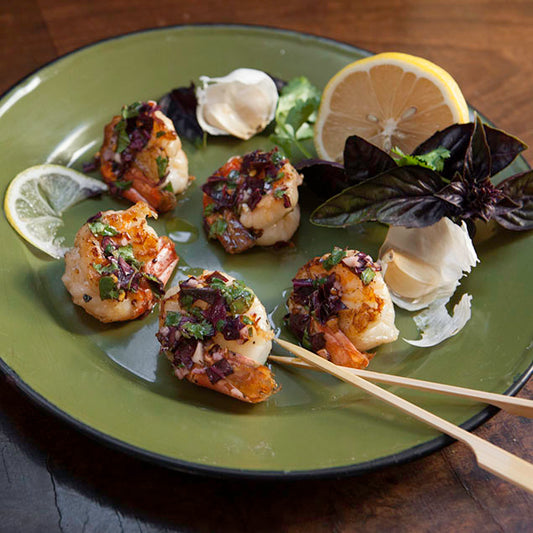 Pasolivo Shrimp with Thai Lemon Basil Vinaigrette Recipe plated with garlic cloves, skewers, and a lemon wedge